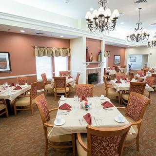 An elegantly set dining room with neatly arranged tables and chandeliers overhead.