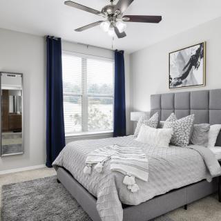 A modern bedroom with a stylish grey and white color scheme, featuring a large bed, elegant curtains, a full-length mirror, and contemporary artwork.