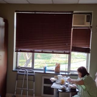 A cozy room with blinds drawn over the window, featuring a person sitting at a table.