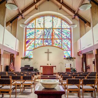 A serene view of a church interior featuring beautiful stained glass windows and a central altar.