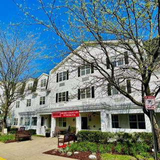 A three-story residential building with a red awning, surrounded by trees on a clear day.