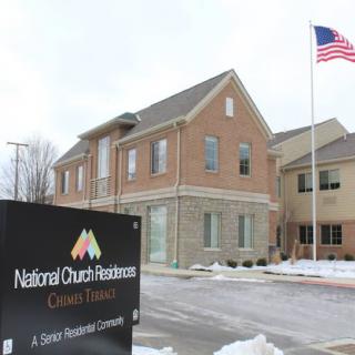 A view of the National Church Residences building with snow on the ground and an American flag flying.