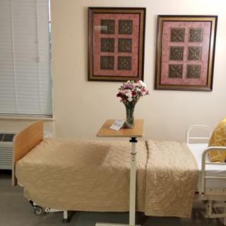 A hospital room with a neatly made bed and flowers on a table.
