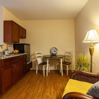 Cozy kitchen and dining area with wooden cabinets, a round table with chairs, a lamp, and small refrigerator.