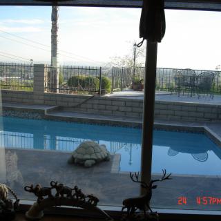 A view of a backyard pool and patio through a window on a sunny day.