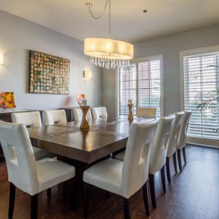 A modern dining room with a large table surrounded by white chairs and illuminated by a stylish chandelier.