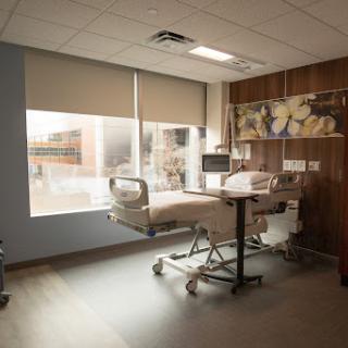 A well-lit hospital patient room featuring a bed, medical equipment, and large windows.