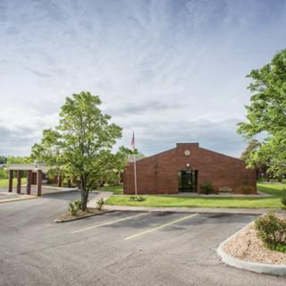 A brick building with a parking lot and surrounding trees on a sunny day.