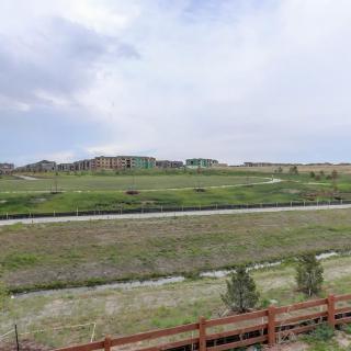 A suburban landscape with a grassy field, cloudy sky, and distant houses.