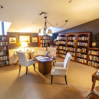A cozy library room with bookshelves, a central table, and comfortable chairs.
