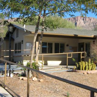 A small desert house with a ramp and surrounding vegetation on a sunny day.
