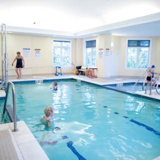 A bright and welcoming indoor swimming pool designed for rehabilitation and water exercises, featuring several individuals participating in activities.