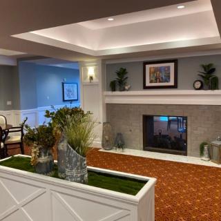 A cozy living room with a fireplace, decorated with plants and artwork.
