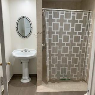A neatly arranged bathroom with a pedestal sink, oval mirror, and patterned shower curtain.