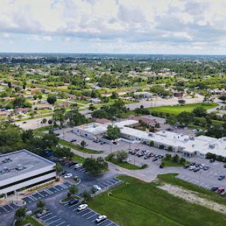 An expansive aerial view showcasing a blend of commercial and residential areas, surrounded by greenery under a partly cloudy sky.