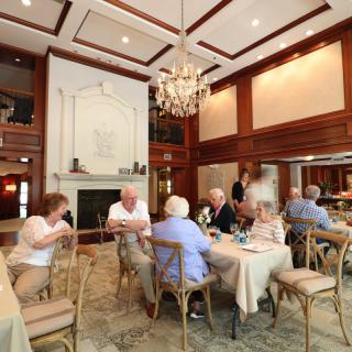 A group of people dining and socializing in an elegant restaurant interior with a chandelier.