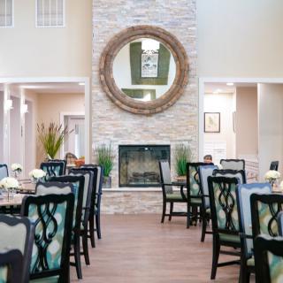 A modern dining room with elegantly set tables, a central fireplace, and a large decorative mirror.