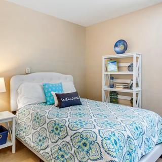 A cozy bedroom with blue and white decor, featuring a bed with patterned bedding and a bookshelf.