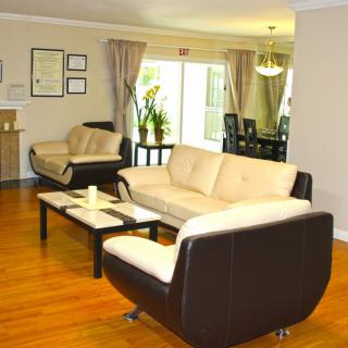A modern living room featuring comfortable sofas, a coffee table, and a view into the dining area with flowing curtains.
