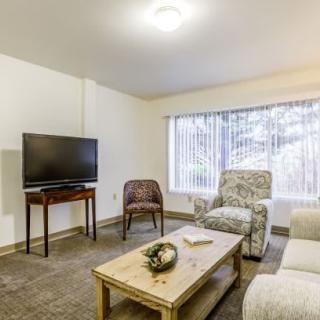A cozy living room with modern furniture, featuring a television, chairs, a sofa, and a coffee table near a large window.