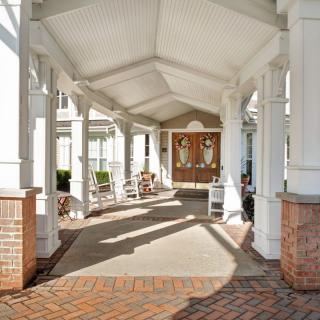 A covered entrance with columns and brickwork leading to a building, featuring outdoor seating along the walkway.
