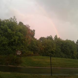 A subtle rainbow appears amidst the stormy clouds and lush greenery.