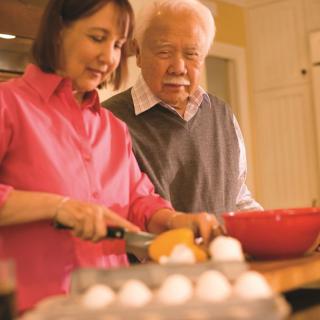 Two people preparing food in a kitchen, one is cutting vegetables while the other looks on.