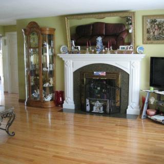 A cozy living room with a traditional fireplace, decorative cabinet, and hardwood flooring.