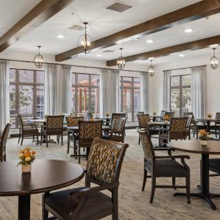 A spacious and elegantly designed dining area with multiple tables and chairs, featuring large windows and decorative lighting.