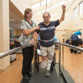 A healthcare professional assists a patient during physical therapy, helping him regain mobility.