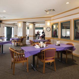 A spacious dining area with tables covered in purple tablecloths and wooden chairs.