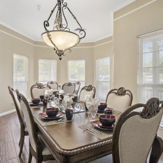 An elegantly furnished dining room with a large table set for a meal, featuring an ornate chandelier and ample natural light from multiple windows.