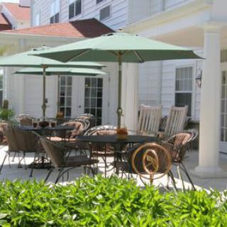 A sunny outdoor patio with wicker chairs and green umbrellas, surrounded by lush greenery.