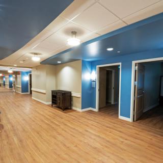 A brightly lit hallway with blue walls and wooden floors, typical of a nursing home interior.