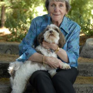 An elderly woman sitting outside with her dog on her lap.