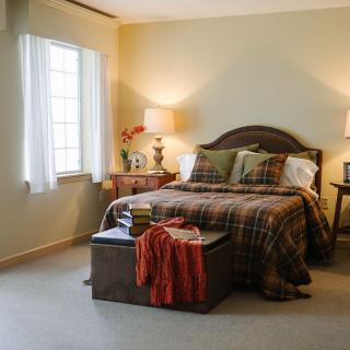 A cozy bedroom with a neatly made bed, side tables with lamps, and a window letting in natural light.
