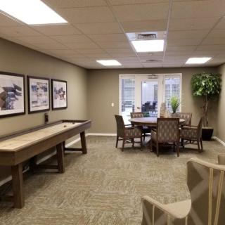 A cozy game room featuring a shuffleboard table, seating area, and framed artwork on the walls.