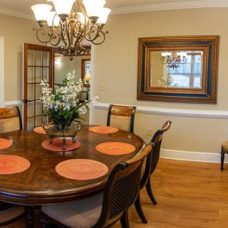 A cozy dining room with a round wooden table and six chairs, decorated with a chandelier and a large mirror on the wall.