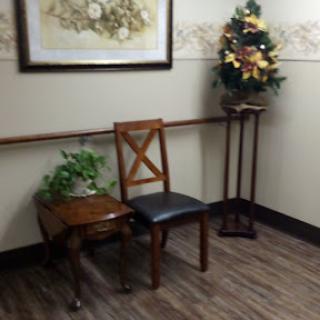 A cozy waiting area featuring a wooden chair, a small table with a decorative plant, and a festive tree.