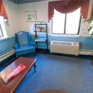 A cozy living room with a blue chair, coffee table, and window with red curtains.