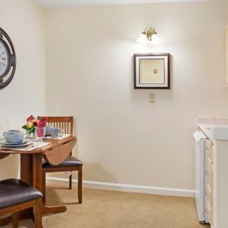 A cozy dining area with a wooden table set for two, accompanied by chairs and decorated with a wall clock and framed art.