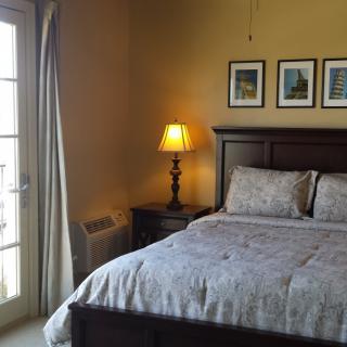 A cozy bedroom with a neatly made bed, nightstand, and lamp beside a window.