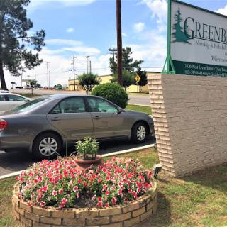 A parked car beside a flowerbed in front of a business sign.