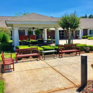 A sunny outdoor area with benches, shrubbery, and a building entrance.