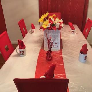 A beautifully set dining table with a red and white theme, featuring a central flower arrangement and creatively folded napkins in mugs.