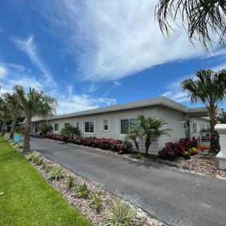 A serene view of a mobile home surrounded by lush landscaping and palm trees under a bright blue sky.