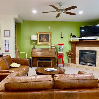 A cozy living room featuring a leather sofa, piano, and a warm green wall.