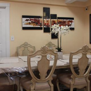 A beautifully decorated dining room with elegant chairs, a large table, and a centerpiece of white orchids under decorative wall art.
