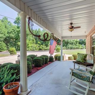 A cozy porch with rocking chairs and an American flag, surrounded by lush greenery.