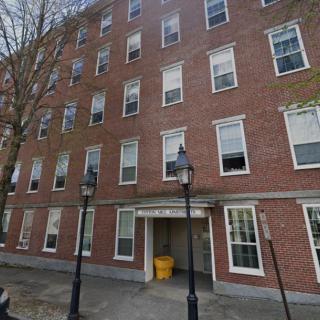A brick residential building with multiple windows and street lamps in front.